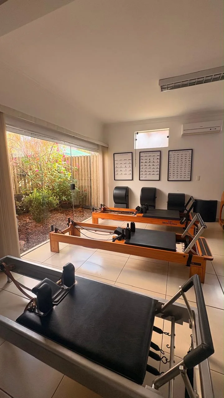 Estúdio de Pilates com reformers clássicos e contemporâneos dispostos em fileira, ambiente amplo com vista para o jardim